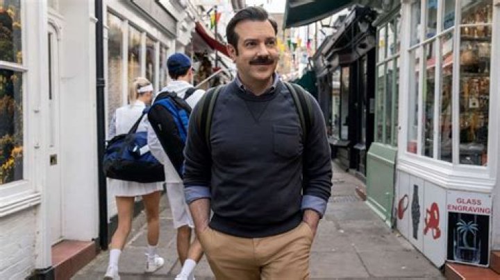 Ted Lasso is walking down the street with a backpack on.
